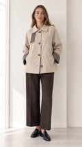 Front view of women's beige short trench jacket with houndstooth trim and dark trousers