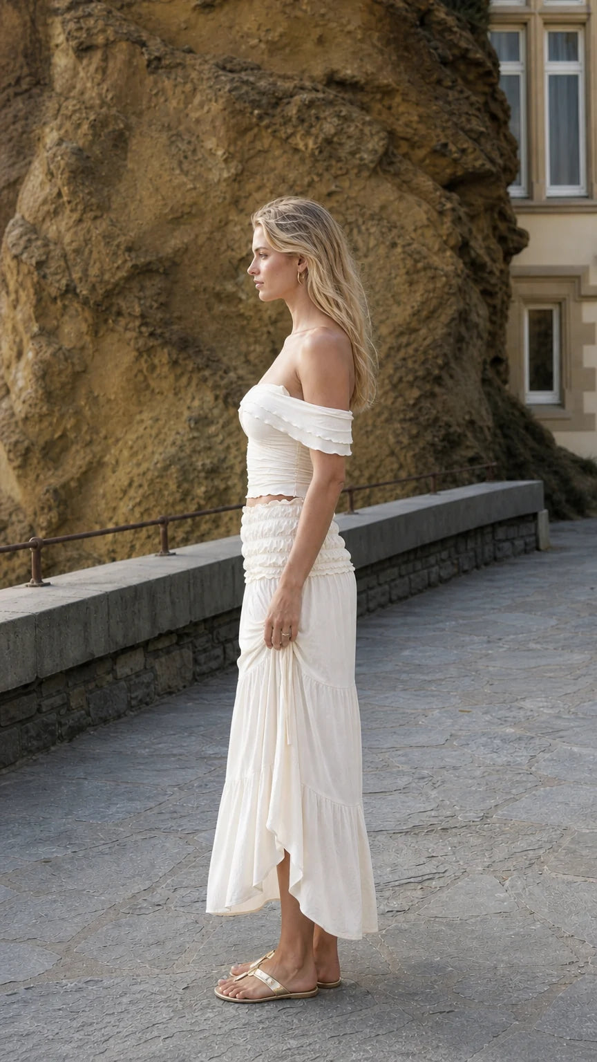 Side profile view of woman in ivory two-piece set standing near stone wall