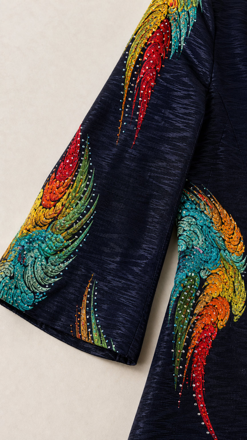 Close-up detail of textured fabric, colorful feather print, and rhinestone embellishments on sleeve