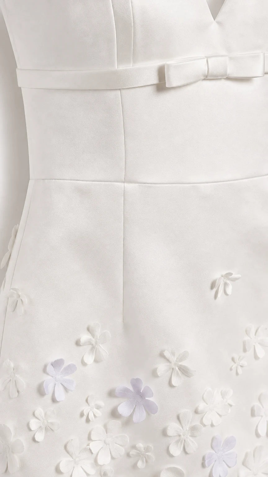 Close-up of white mini dress bodice bow and 3D floral hem