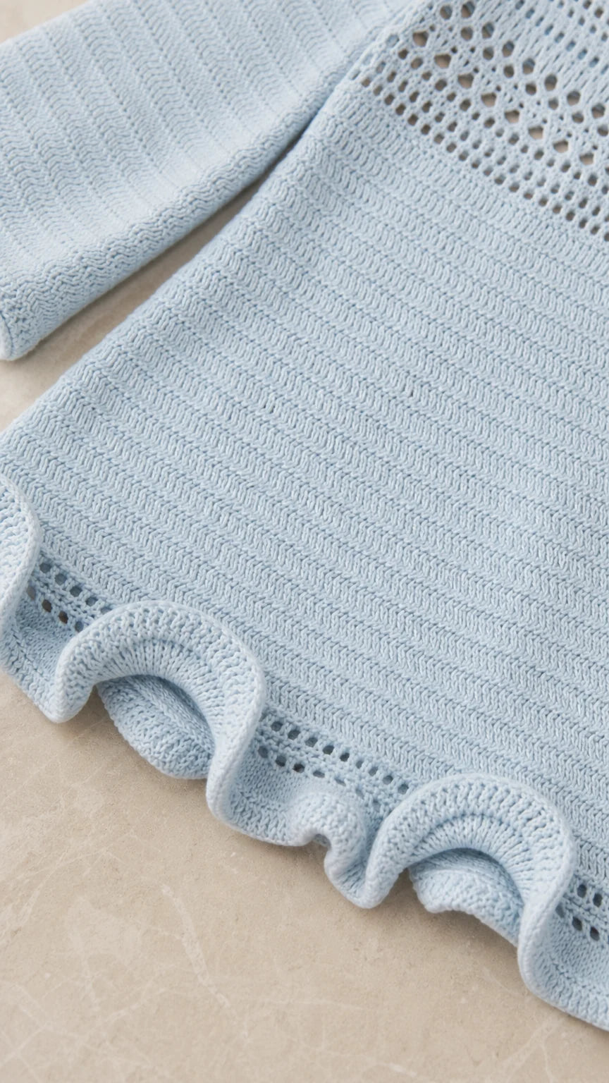 Close-up detail of the open-knit sleeve and ruffled hem in light blue